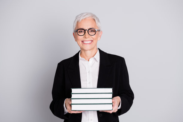 照片肖像可爱的退休女士大学教授拿着书穿着正装眼镜孤立的灰色背景图片下载