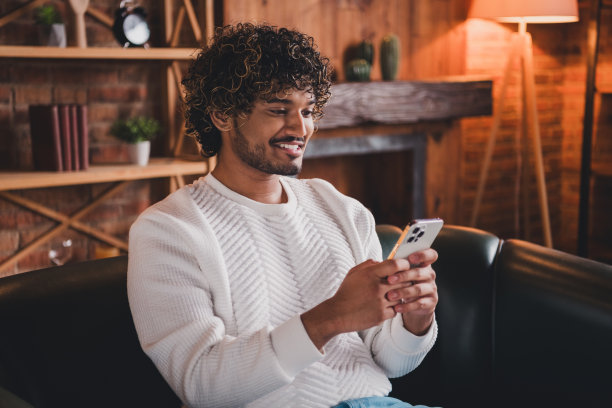 照片英俊的好心情的家伙穿着白色运动衫聊天苹果三星iphone设备在室内房间家里的房子图片下载