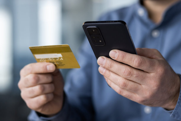 身体某个部位的特写照片。一个穿着蓝色衬衫的年轻商人的手，手里拿着信用卡，拿着手机图片下载