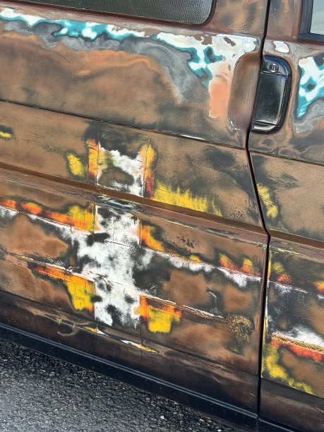 这是生锈的车门的特写图片，车门被喷上了涂鸦，又被打磨掉了，棕色、黑色、黄色、橙色和白色的油漆颜色，柏油路地板，聚焦在前景上图片下载