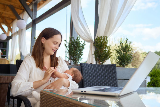 忙碌的母亲抱着婴儿，用电脑在咖啡馆里处理自由工作，代表着商业和育儿相结合的现代生活方式图片下载