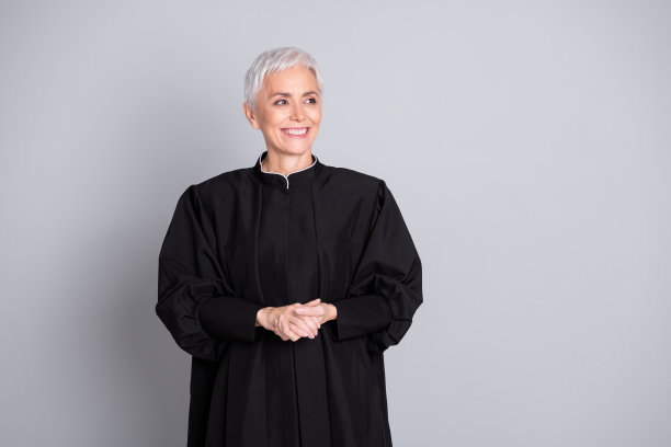 照片中法官面带微笑的老妇人看起来空无一人，穿着黑色长袍孤立的灰色背景图片下载
