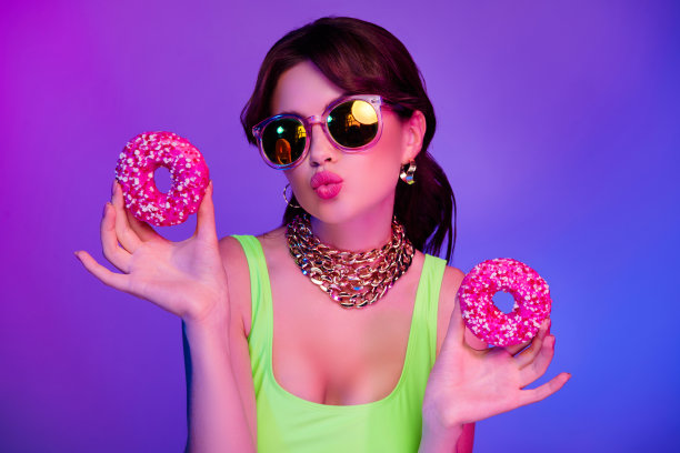 照片中的女孩戴着太阳镜送飞吻，拿着两个美味的饼干，隔绝了紫外线的颜色背景图片下载