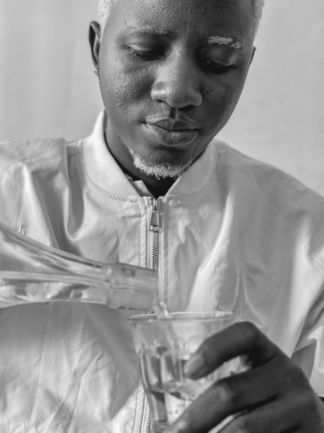 图为一名白发胡须的黑人男子在室内用瓶子喝水。与有色人种的黑白摄影。图片下载