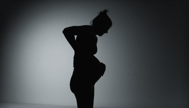 孕妇临产的剪影。她疼了，摸了摸肚子。以黑色背景拍摄。图片下载