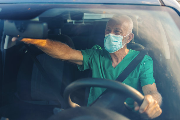 白人男医生在开车。成熟的微笑护士下班后开车回家。白天开车时，戴着医用服和口罩的自信的医务人员。男性医疗保健专业人员开车上班。图片下载