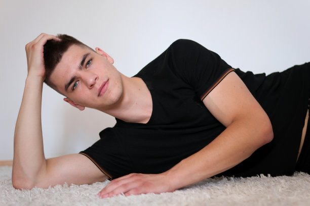 男人躺着看着镜头。穿着黑色t恤，蓝眼睛的帅哥靠在胳膊上躺着图片下载