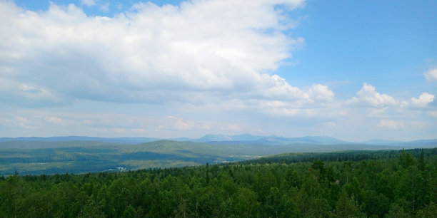 大自然的照片。穿越森林。塔加奈国家公园，俄罗斯。风景与山谷在雾后的森林在一个长满草的小山上。明亮的蓝天上飘着蓬松的云。自然清新概念图片下载