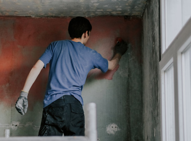 一个年轻人用刷子把红水泥涂在墙上。图片下载