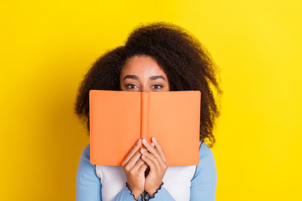 照片中，迷人的年轻女子读着书的封面，脸上穿着时髦的蓝色衣服，孤立在黄色的背景上图片下载