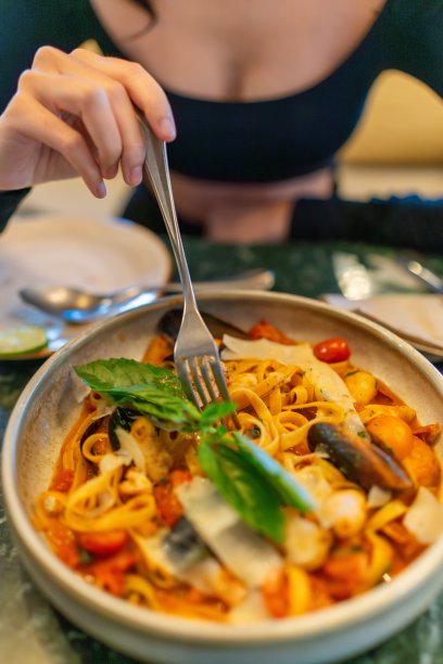 一个亚洲女人在餐桌上吃一盘海鲜面食的特写图片下载