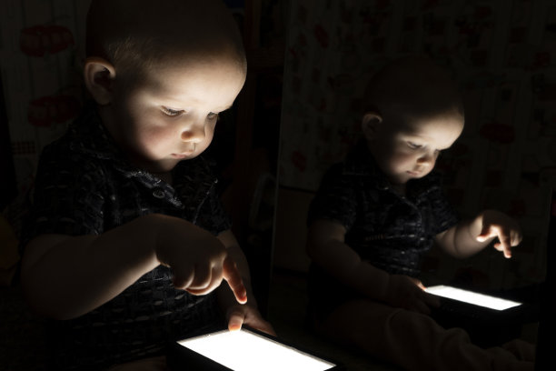 一个小孩坐在黑暗中，看着一块发光的平板。图片下载