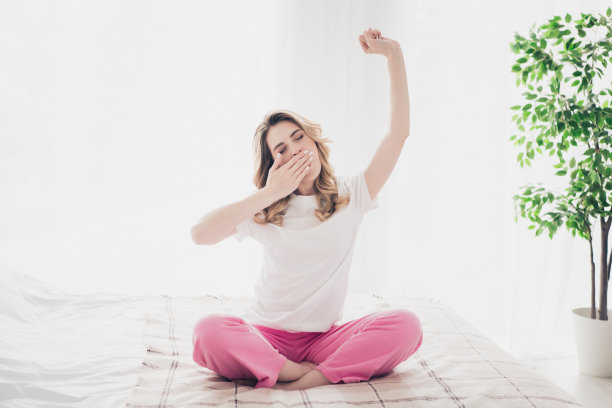 照片中的女孩坐在床上打哈欠，在白色的室内房子里伸开双手图片下载