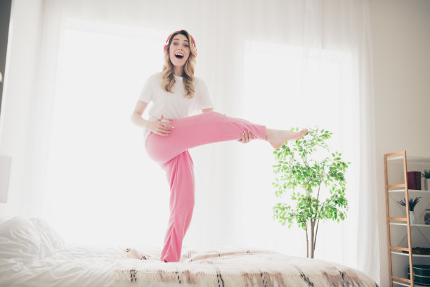 时髦的疯狂女孩站在床上跳舞，在卧室里弹奏梦想腿吉他的照片图片下载