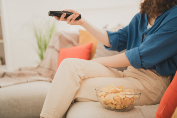 剪短的照片快乐的年轻女孩看电影，坐在沙发薯片零食蓝色衬衫享受生活的新公寓房间，光的房子，平的室内图片下载