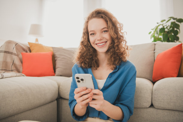 迷人时髦的年轻女子的照片坐在地板上，手持设备蓝色衬衫移动新公寓的室内室内图片下载
