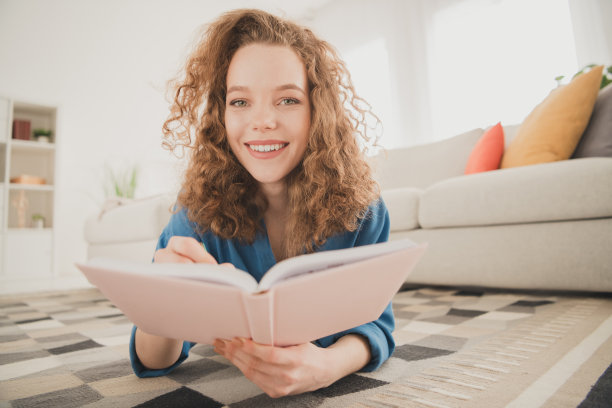 快乐的年轻女孩的全尺寸照片躺在地板上写笔记本蓝色衬衫享受生活的新公寓房间灯光房子公寓室内图片下载