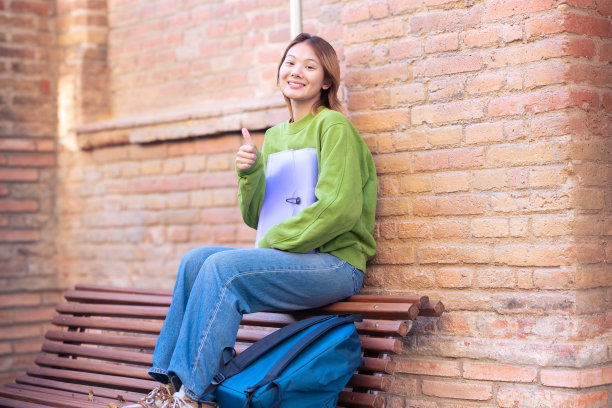 一个快乐的中国年轻女子在户外拿着笔记本的照片。图片下载