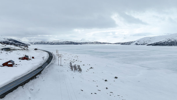 鸟瞰部分冻结的峡湾和雪山冬季景观在挪威，道路在雪景图片下载