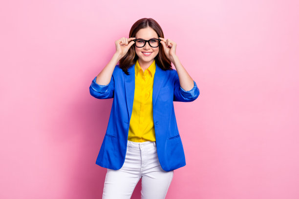 照片中，年轻、开朗、满意、微笑的女商人穿着时髦的休闲办公装，在粉红色的背景上试着戴上她的新眼镜图片下载