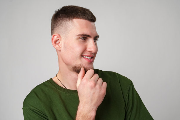 穿着绿色t恤的短发年轻人把手放在下巴上摆姿势图片下载