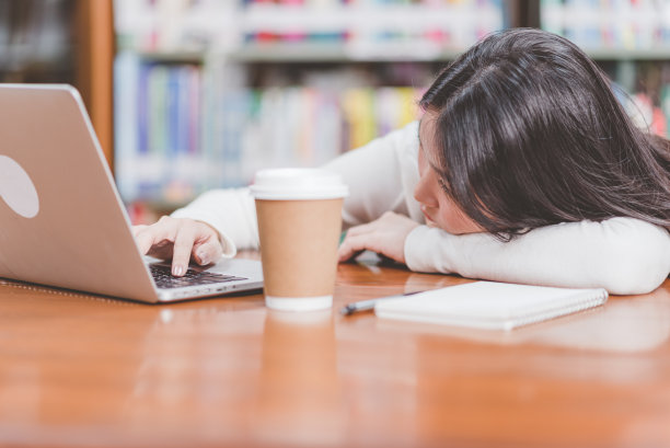 照片中的人看起来很累，或者在用笔记本电脑工作时很难保持清醒。一杯咖啡放在旁边，表明照片中的人正试图保持清醒。图片下载