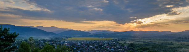 全景美景与蓝天。春天的夕阳在村庄上空。有田野和山脉的乡村景观。照片的背景是村庄的景色和阳光。图片下载