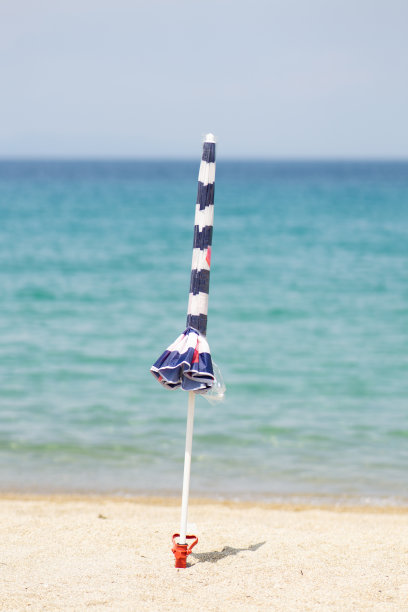 在沙滩上一把闭合的沙滩伞的垂直照片，背景是蓝色的大海和天空图片下载