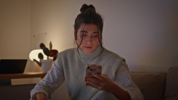 女玩家看智能手机，晚上把游戏手柄放在沙发上图片下载