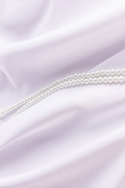 美丽的垂直婚礼背景与一串珍珠珠在白色缎面织物柔软的褶皱。垂直的背景。空间的副本。图片下载