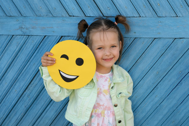 有趣快乐的漂亮女孩抱着一个微笑的黄色笑脸。通过表情符号传达情绪图片下载