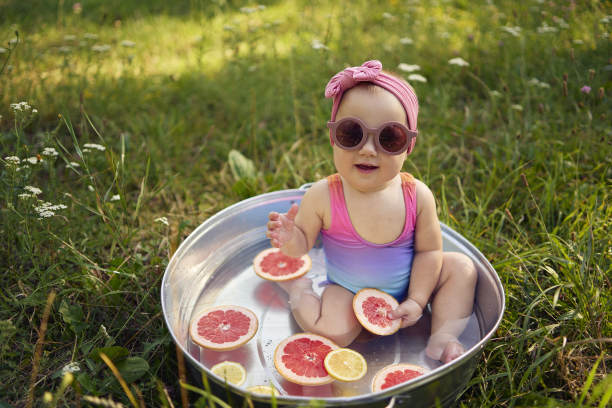 一个戴着墨镜的婴儿在夏日花园的金属浴缸里玩柚子和柠檬片图片下载