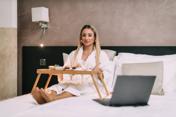 一个女人在床上用笔记本电脑，在酒店房间里吃早餐图片下载