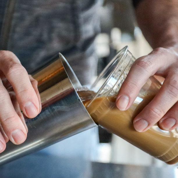 男咖啡师的手从摇壶中倒入棕色奶油咖啡冷萃到透明塑料杯的特写图片下载