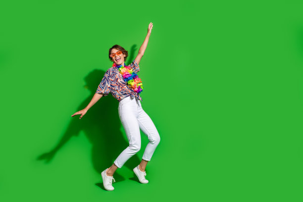 穿着印花衬衫项链，戴着太阳镜，踮着脚尖在绿色背景上跳舞的女人的全身照片图片下载