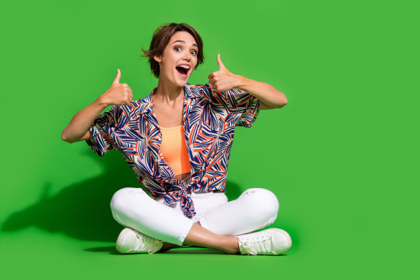 印象深刻的正面女士穿着印花衬衫的全长照片显示两个大拇指向上空的空间孤立的绿色背景图片下载