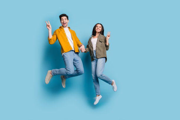 全身照片迷人的好心情女士男士穿衬衫跳高显示v字空间空旷孤立的蓝色背景图片下载