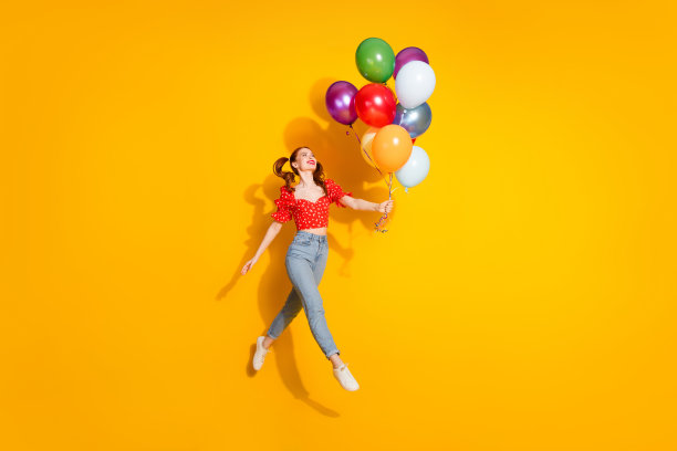 照片中年轻的红头发积极的女孩穿着衬衫和牛仔裤，拿着气球，在黄色的背景上孤独地庆祝派对图片下载