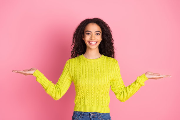 年轻女孩的肖像照片在绿色套头衫拿着两个产品空的空间平衡提供孤立的粉红色背景图片下载