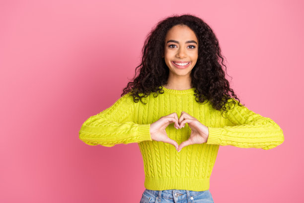 年轻女孩的照片肖像，波浪的深褐色卷发，穿着绿色的毛衣，在粉红色的背景上做-爱的象征图片下载