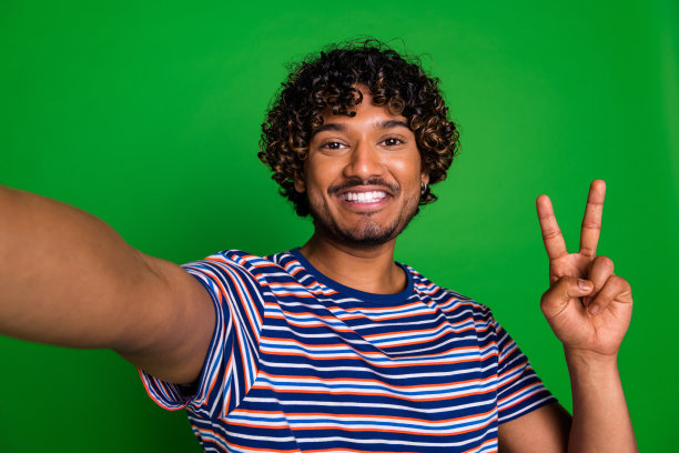 照片的酷积极的好男人穿时髦的条纹衣服视频直播v标志孤立的绿色背景图片下载