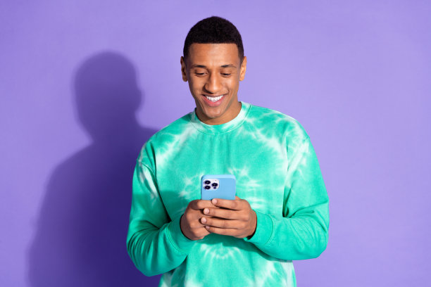 照片英俊的好心情的家伙穿着蓝绿色的运动衫发短信instagram推特电报facebook孤立的紫色背景图片下载