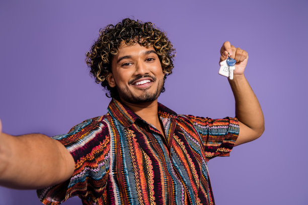 照片的好积极的男人与胡子波浪发型穿着印花衬衫拿着钥匙使自拍孤立的紫色背景图片下载