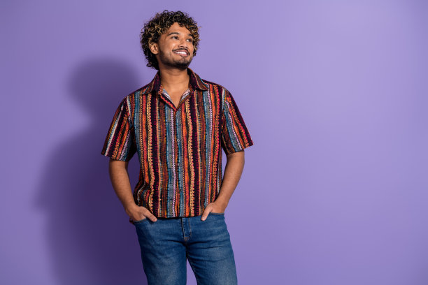 照片英俊的男子波浪发型穿着印花衬衫手臂在口袋里看着销售空空间孤立的紫色背景图片下载