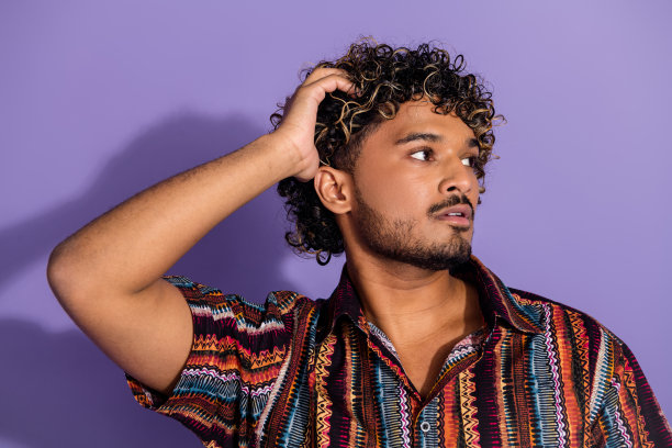 照片英俊的男人与胡子触摸波浪发型穿着印花衬衫看标志空白空间孤立的紫色背景图片下载