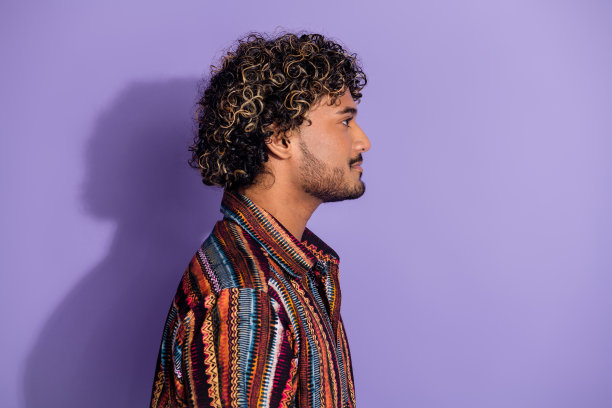 有胡子的严肃男人的侧面照片，穿着印花衬衫牛仔裤，在紫色的背景上提供孤立的空间图片下载