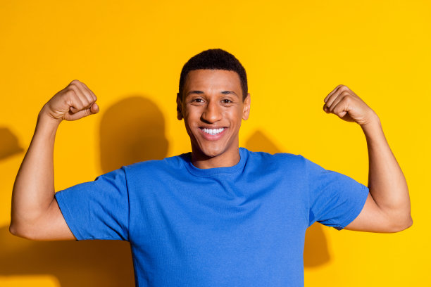 漂亮的年轻男性的照片肖像显示肌肉二头肌穿着时髦的蓝色衣服孤立的黄色背景图片下载