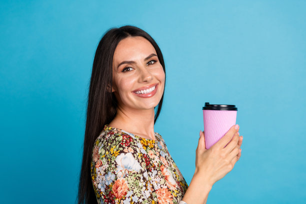 照片中心情愉快的女士穿着印花衣服享受着饮料，空旷的空间孤立的蓝色背景图片下载