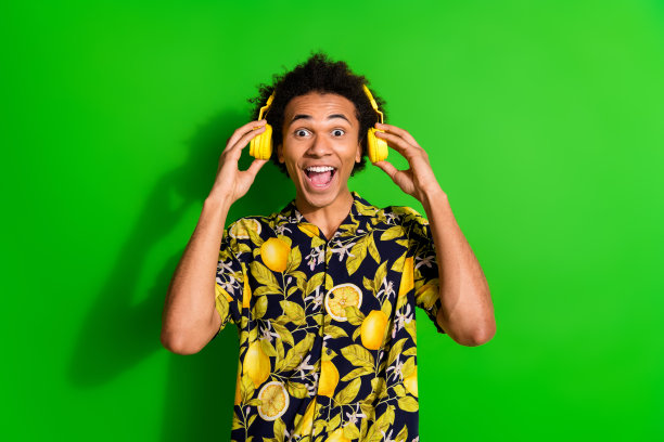 欢快兴奋的酷男照片，穿着时髦的夏装，在绿色的背景上听着孤立的音乐图片下载