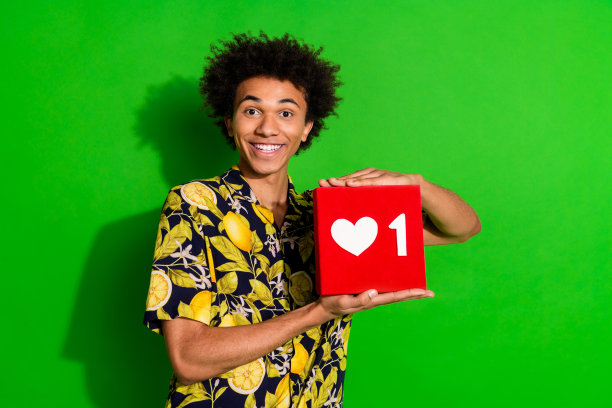 照片中，开朗开朗的好男人穿着时髦的热带印花衣服，手拿红牌孤立在绿色背景上图片下载